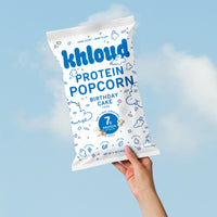 White bag of Khlouds birthday cake flavored protein popcorn held against blue sky background.