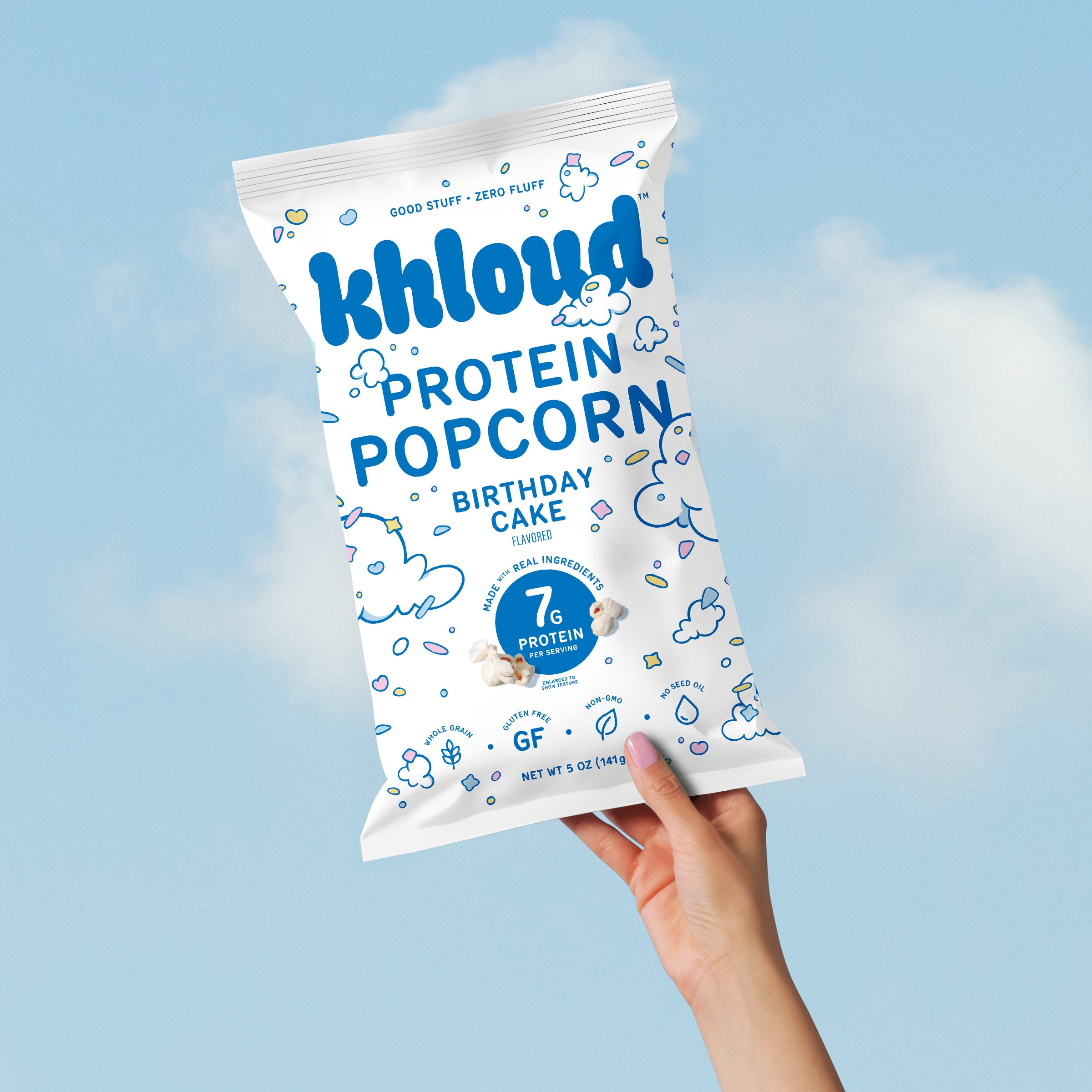 White bag of Khlouds birthday cake flavored protein popcorn held against blue sky background.